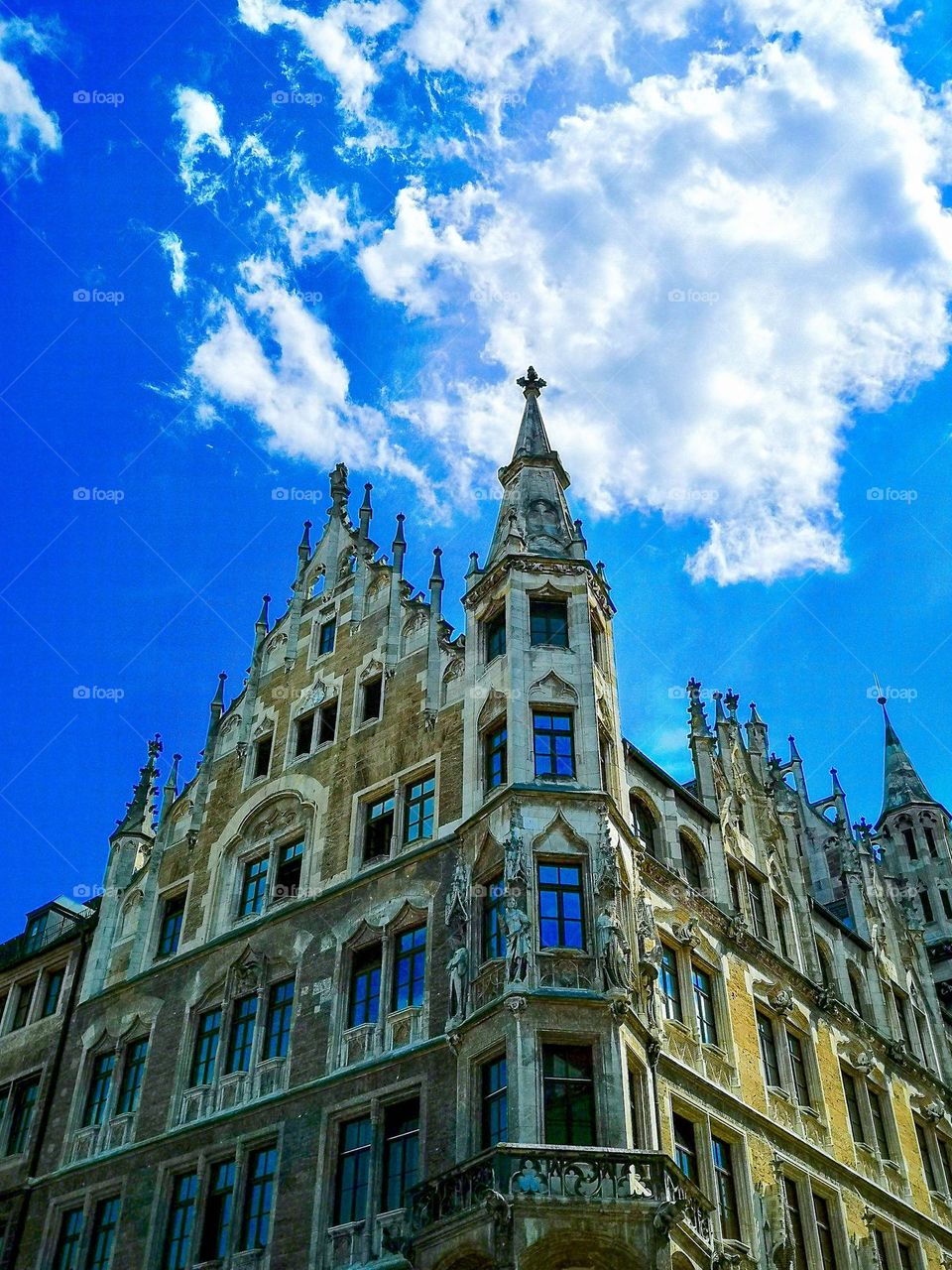 A low angle photo of one side of the Munich new city hall. Blue sky with a nice cloud cover. The building is designed with Gothic Revival architecture.