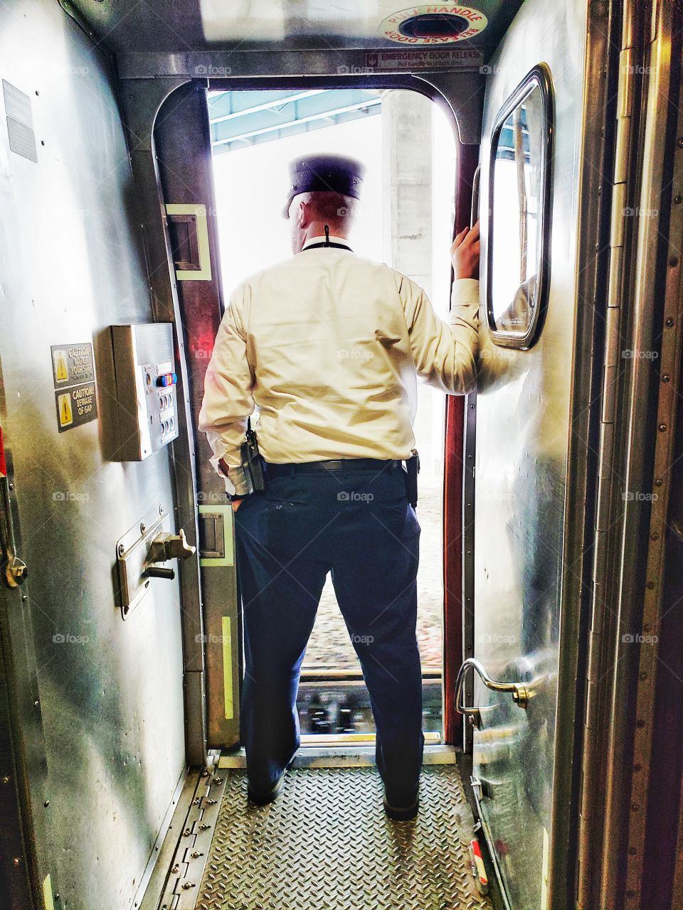 A Male train conductor stands in an open doorway of a train car.