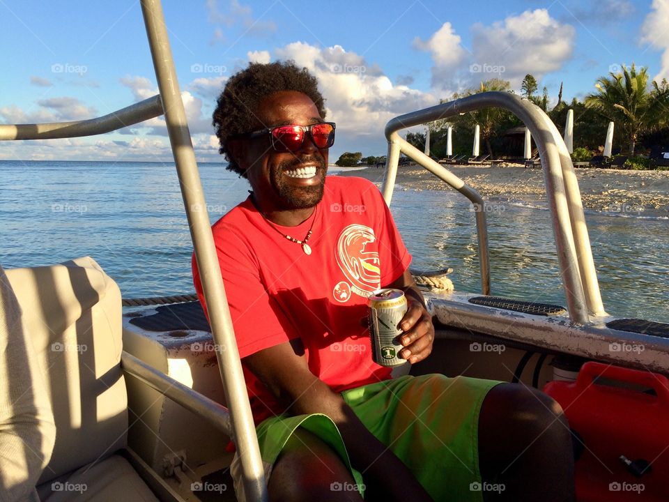 Happy man with sunglasses on a boat at the sunset holding a beer