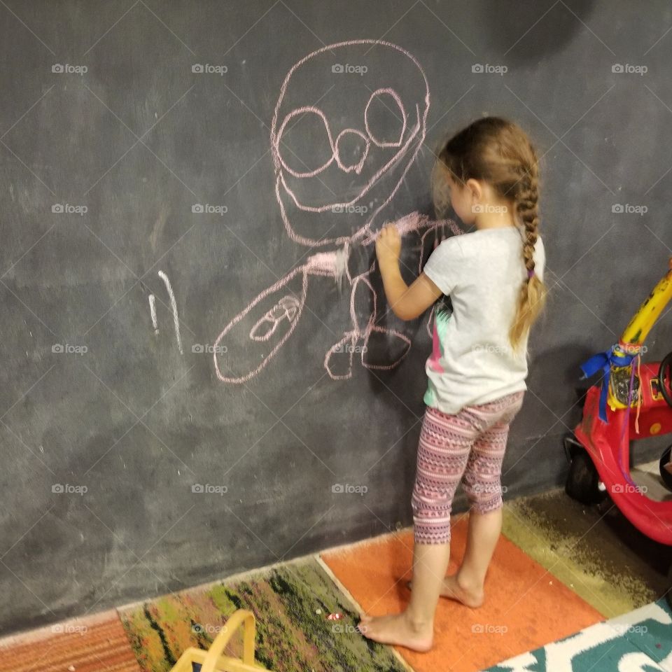 girl student drawing child's figure on chalkboard. bare feet, free play. art imagination.