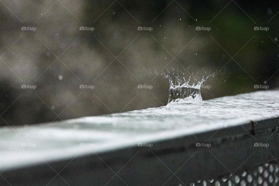 A rainy day leads to many raindrops splashing on a metal rail