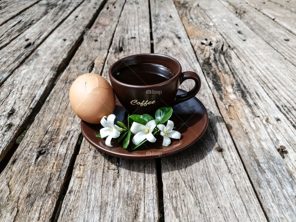 Cup of black coffee with boiled-egg and white flowers