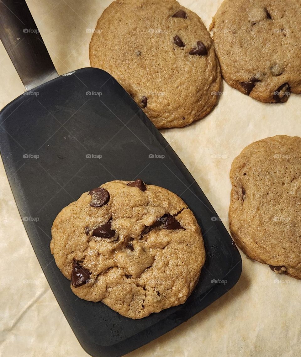 freshly baked chocolate chip cookie lifted off the tray by a black spatula in a home kitchen