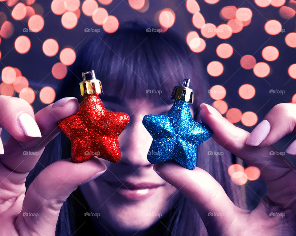 Portrait of a young smiling woman holding glittering red and blue Christmas tree decorative stars in front of night lights 