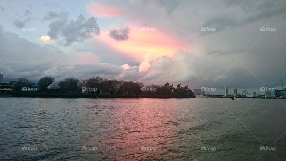 Low sun creating a pink hue between clouds, reflected on the River Thames at Greenwich, London
