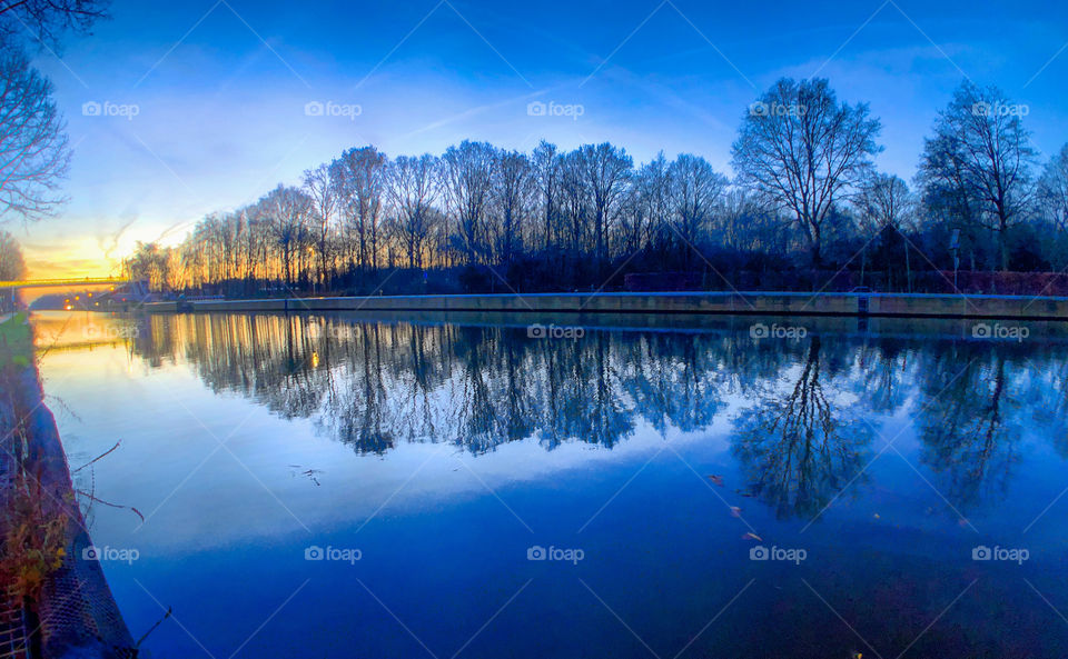 Deep blue winter sky with an early rising sun reflected in the water of a river