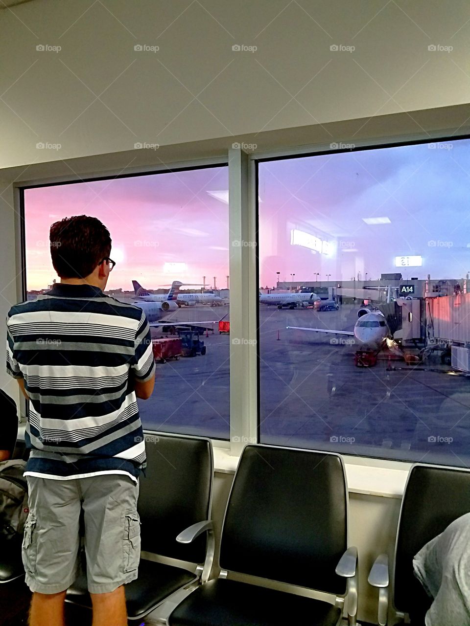 young man looking out window at airport at sunrise