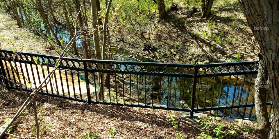 a black railing in front of a stream flowing alongside a small path
