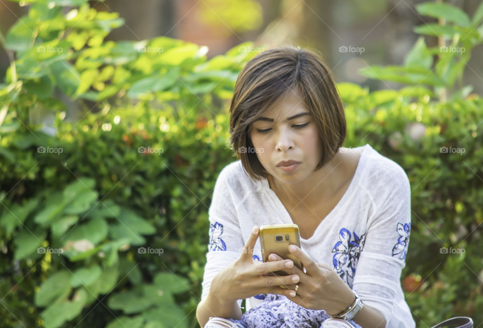 Asian women Sitting on the sidewalk along the street and play Mobile.