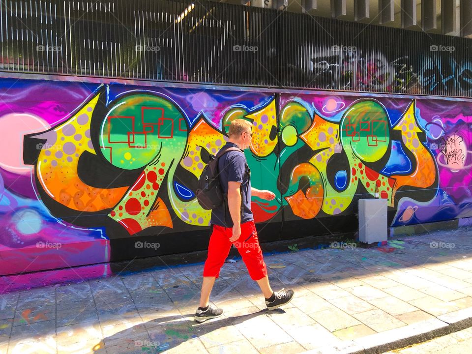 A male walking near the colorful graffiti wall