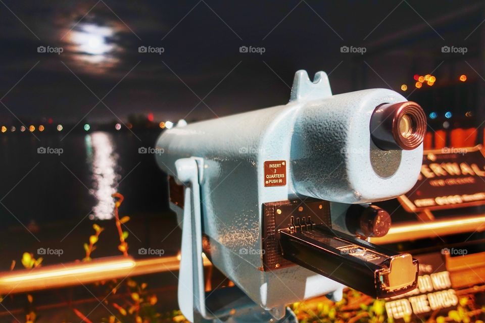 Paid telescope for boat watching across the Mississippi River. Night view with background moon. Along the Outlet Collection by Riverwalk. New Orleans, Louisiana, USA.