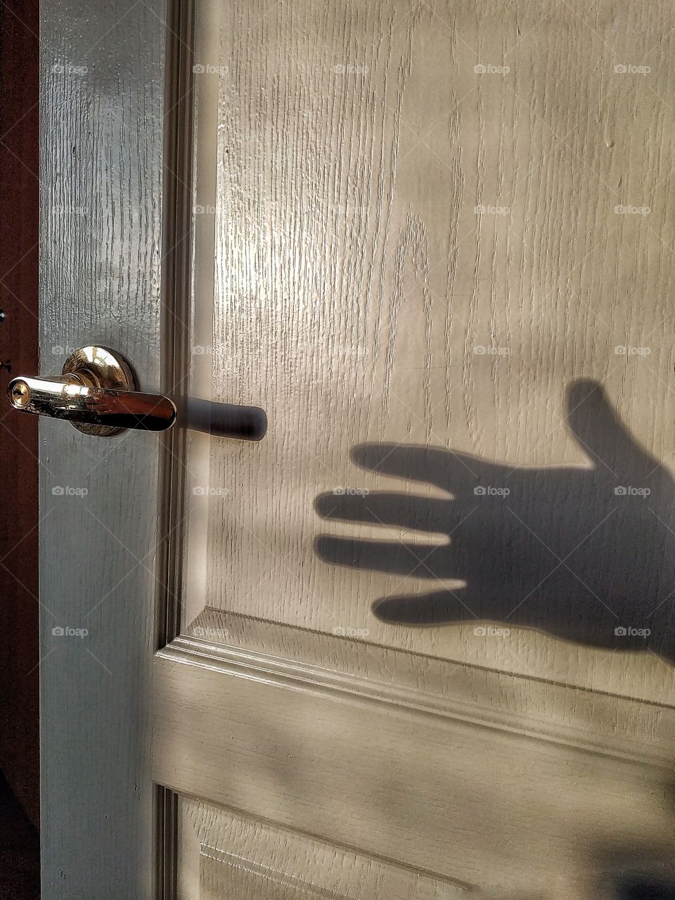 The shadow of a hand, reaching for the door handle