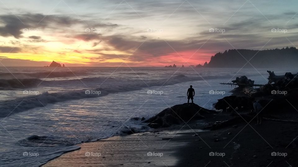 Silhouette of a man standing on an epic rugged coastline with a vibrant post sunset glow in the sky. 