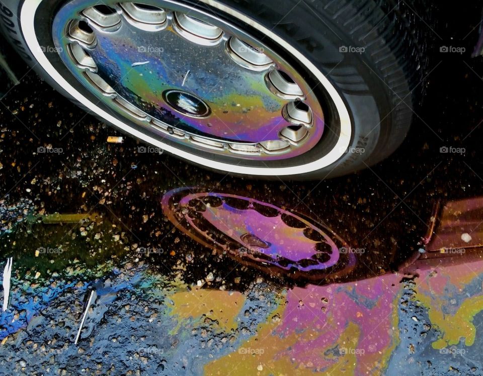 After a rain a reflective image of oilslick in a parking lot. The by products of our automobiles.