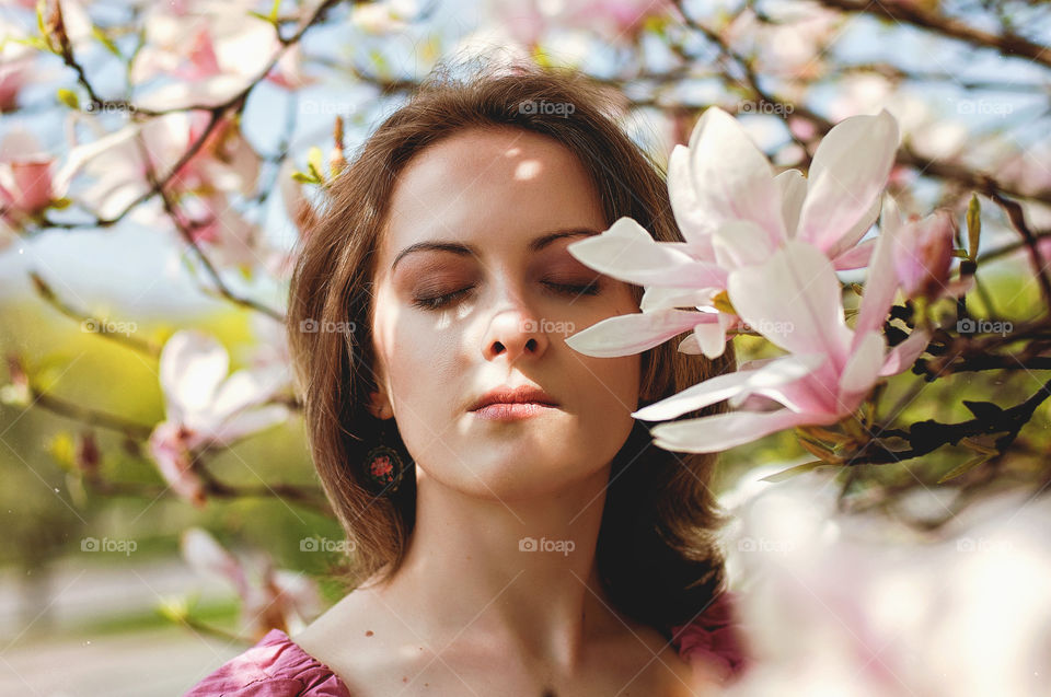 Beautiful portrait of young caucasian girl in pink dress in spring garden with blooming magnolias.