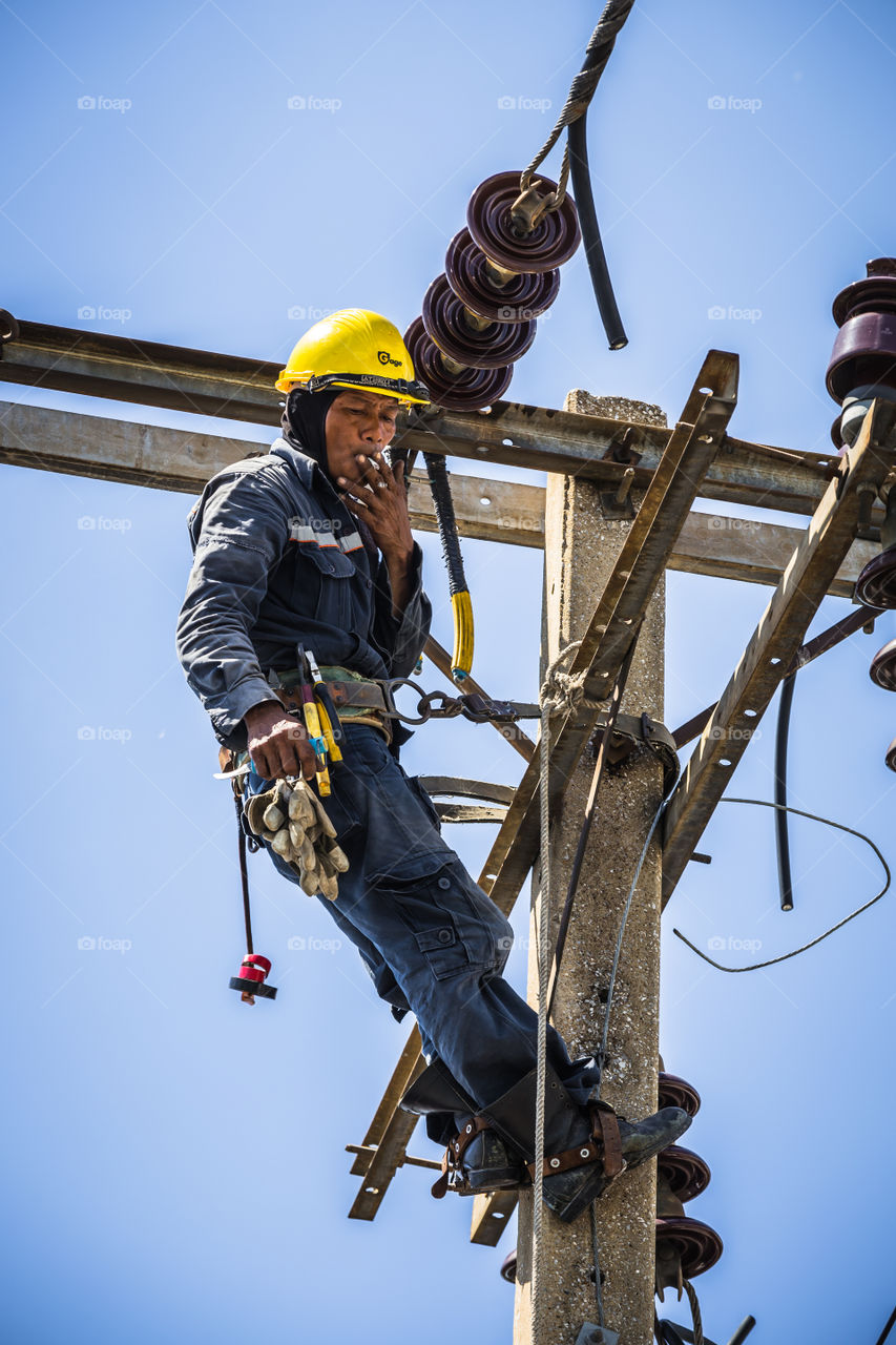 Electrician smoking while working on the electricity pole to replace the electrical insulator