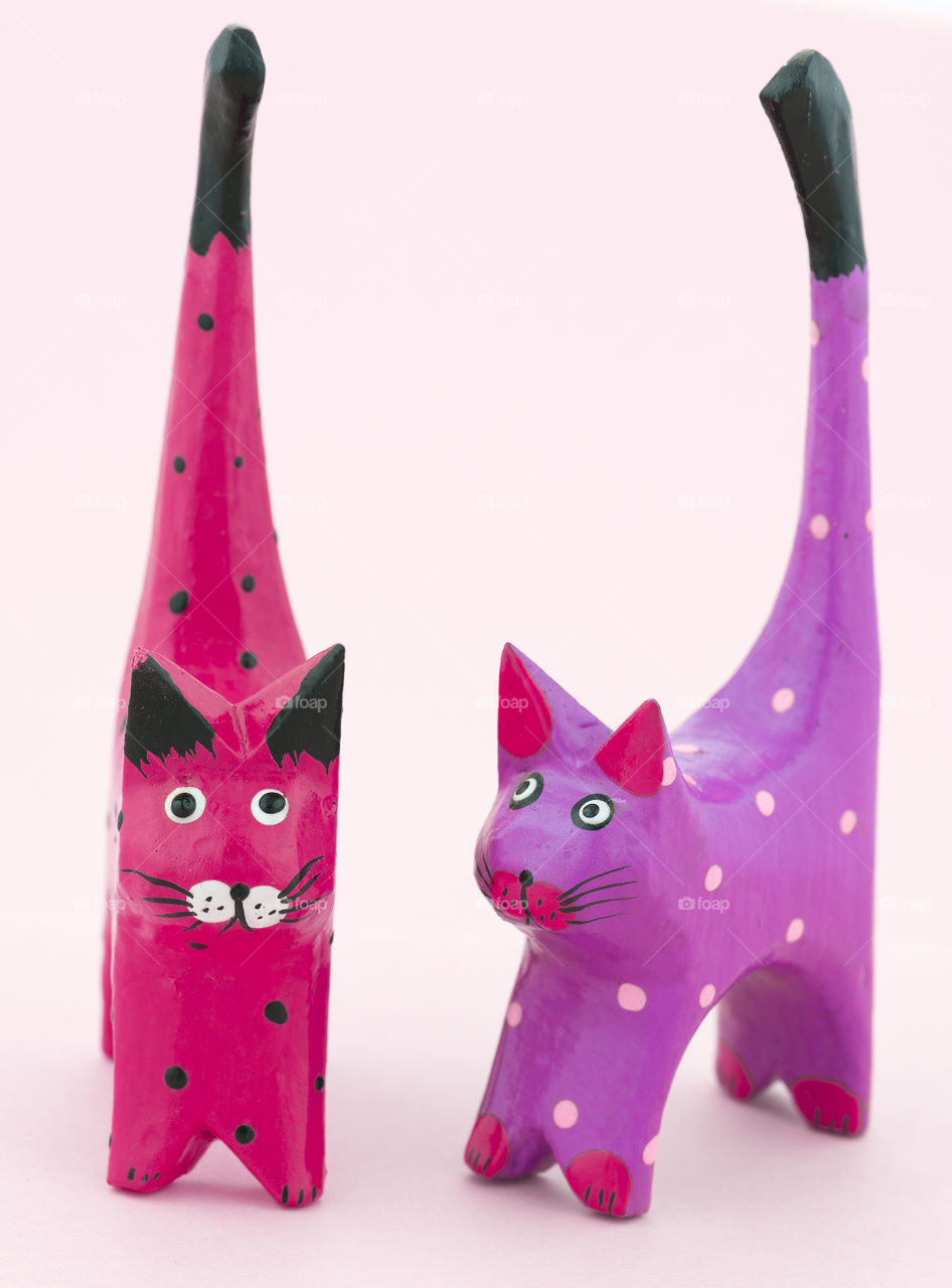 Pink and purple wooden cats on a pink background.