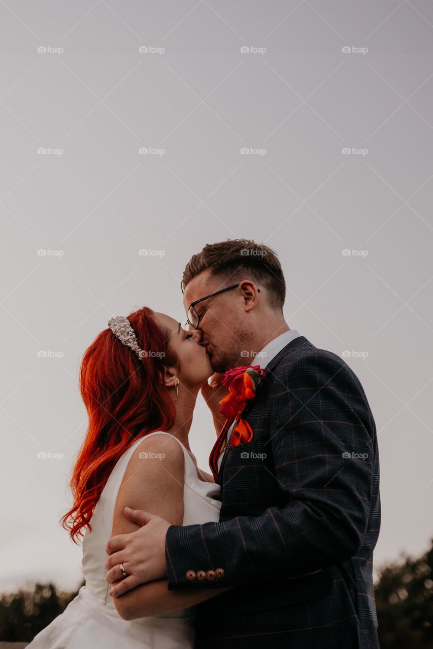 Couple sharing a romantic kiss on their wedding day at sunset 