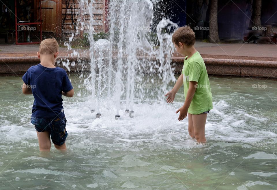 children boys in the water splash fountain, summer heat, city street view