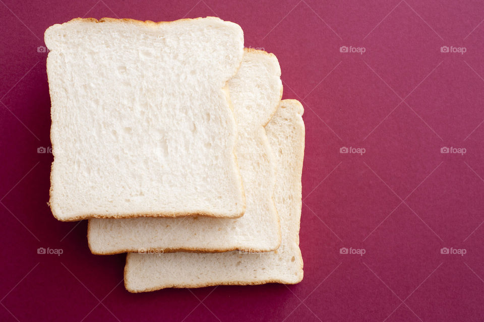 Top view of three slices of bread, one on top of another, on red background
