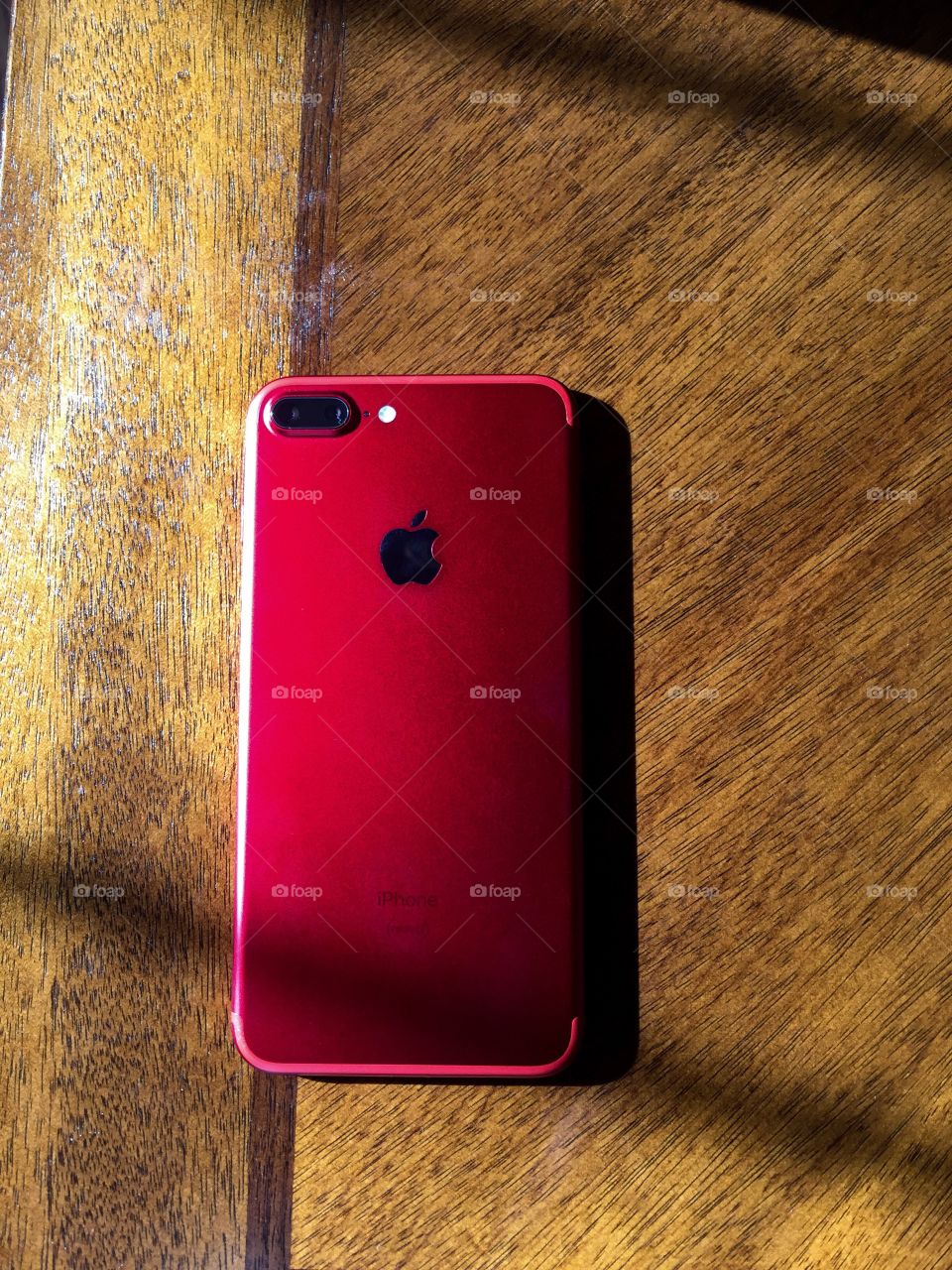 This is an iPhone 7 Plus Red special edition. It's for HIV awareness. I guess a certain percentage goes to organizations that promote awareness of HIV. This phone was bought with a good cause in mind. I had taken the photo with an iPhone 6 Plus. This smart phone has two rear cameras with an led light next to it. It's sitting on a wooden table with sunlight coming in on its side through the window . I love this phone and encourage you to go buy it