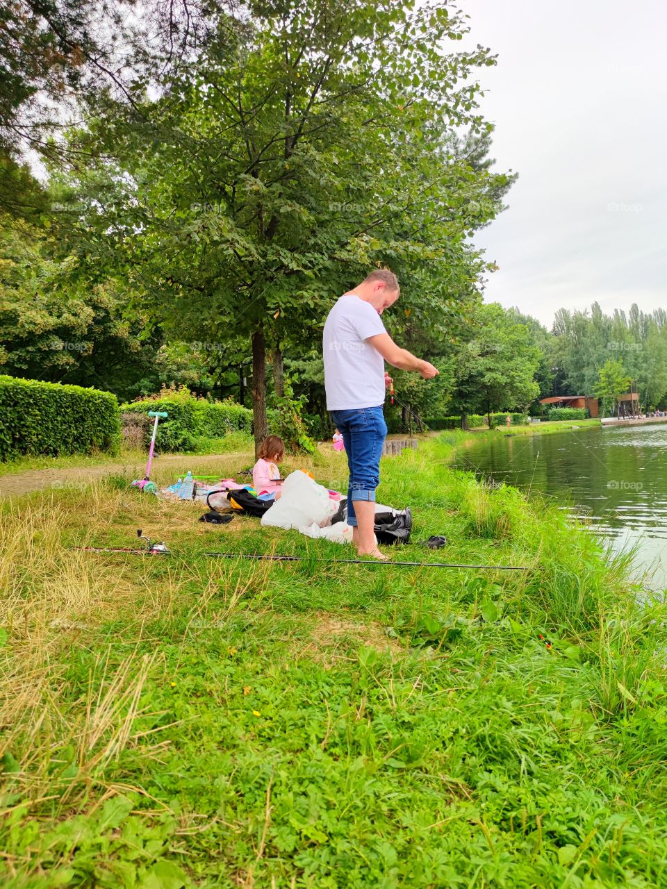 Summer rest.  green coast.  a man equips a fishing rod to catch fish.  A little girl is sitting on a blanket