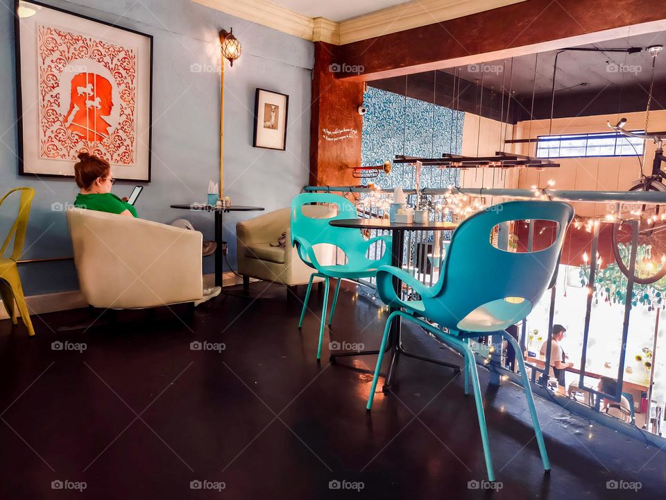 red-haired woman looking at her cell phone sitting in an armchair in a coffee shop, with ornate tables and in a highly decorated place.