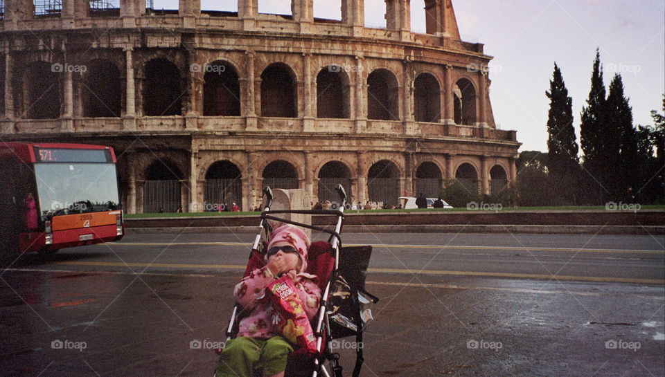 Little girl in stroller eating chips in front of the Colosseum in Rome.