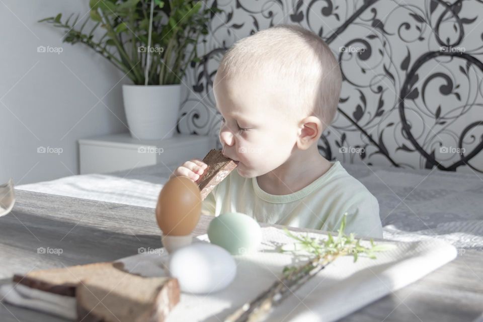 A little boy celebrates Easter, sits at a wooden table and eats