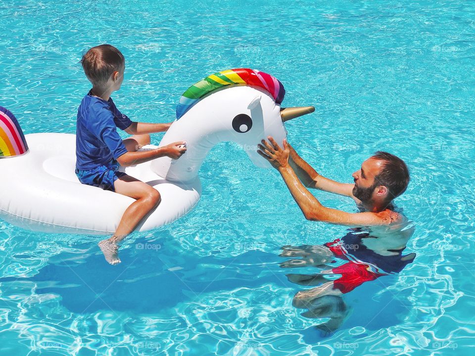 Father and son with unicorn are swimming in the pool