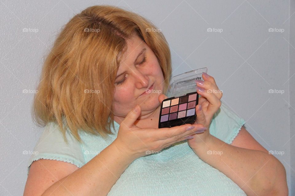 Blonde young woman admiring product, hands holding eye shadow box