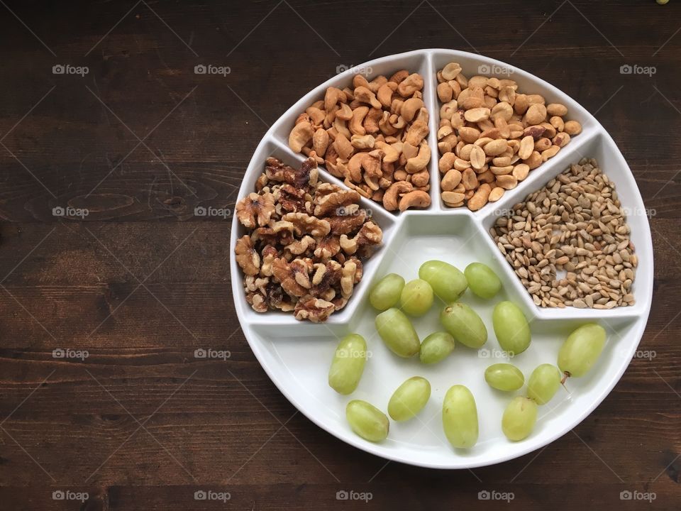 Nuts seeds and grapes (fruit) on a “think Swiss” snack board plate made of porcelain. Great fall and winter healthy health snack that lasts well out on the table. Dark stained wood background. Plate positioned to right in photo (available photo with plate positioned in the centre - can recreate with any items)