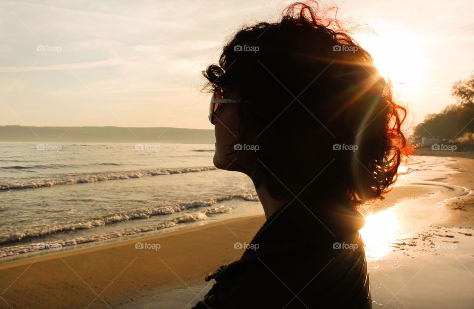 Silhouette of a woman with curly hair looking at the sea, side view, sunlight, sunbeam, sunrays, sunset
