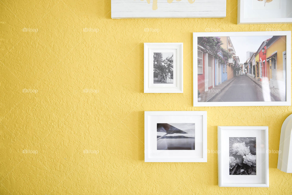 Composition of white framed pictures hung on a yellow wall with negative space