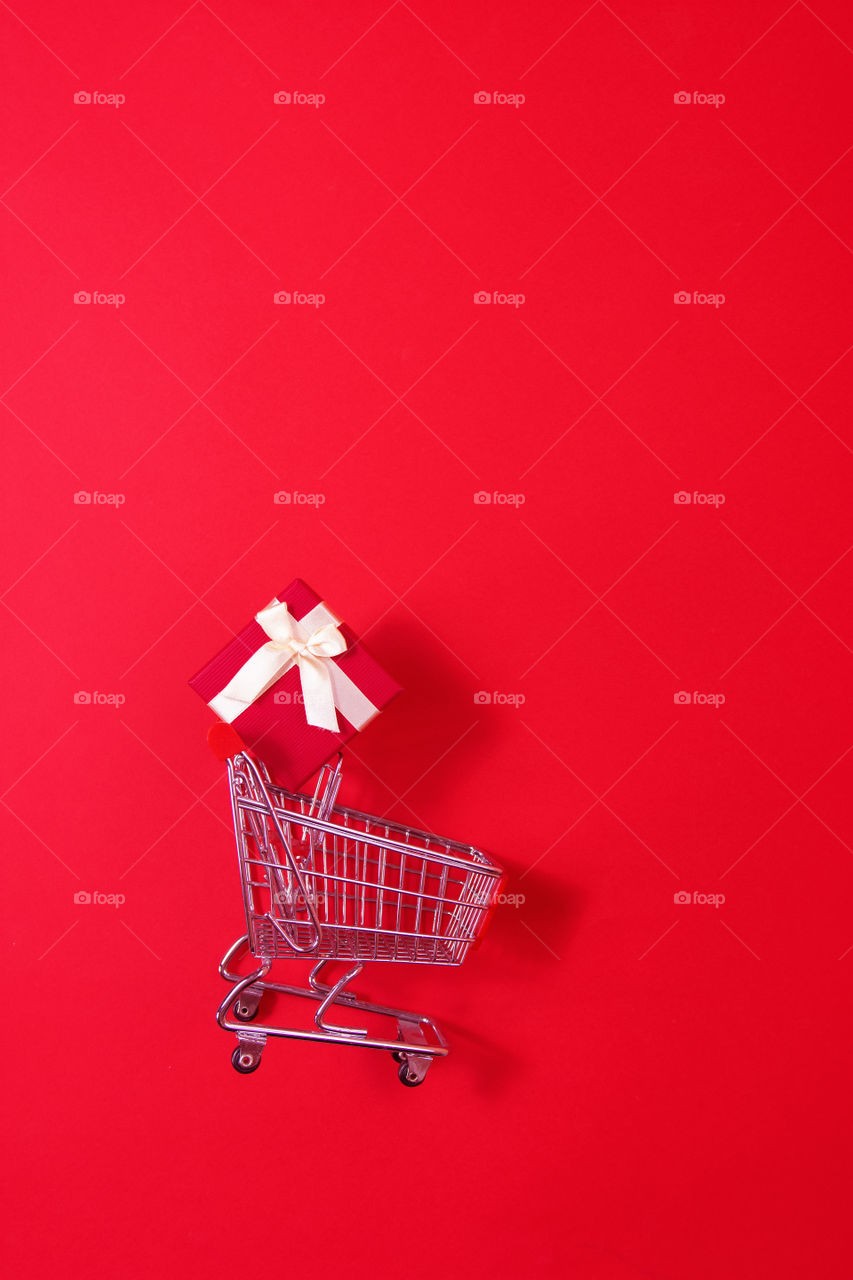Valentine's day shopping concept. Shopping trolley with red gift box on red background. Space for text,top view,copy space ,flat lay,