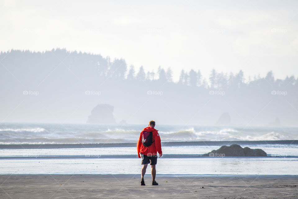 A man in an orange jacket strolling along the beach 