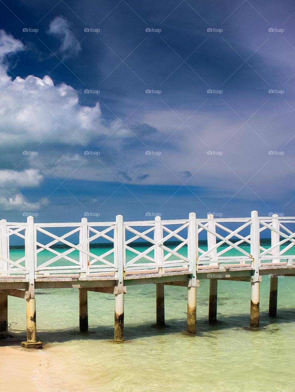 Bright white pier in front of a blue sky and green ocean 