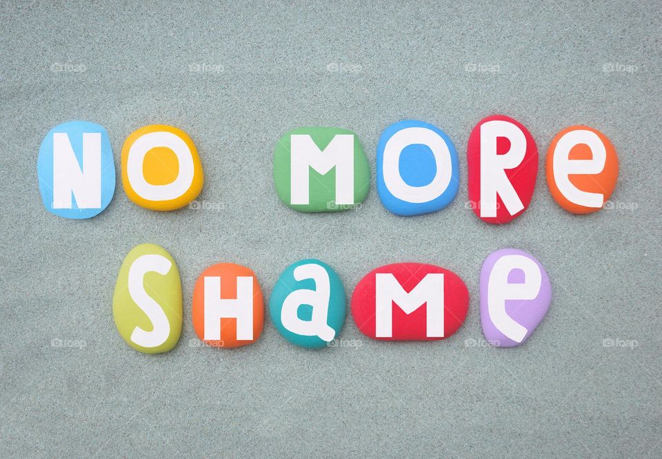 No more shame, social slogan design composed with multi colored hand painted stone letters over green sand