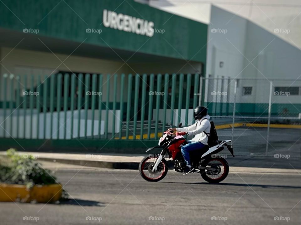 Man with helmet equipped, riding a motorcycle to urgencies, near of an urgencies hospital.