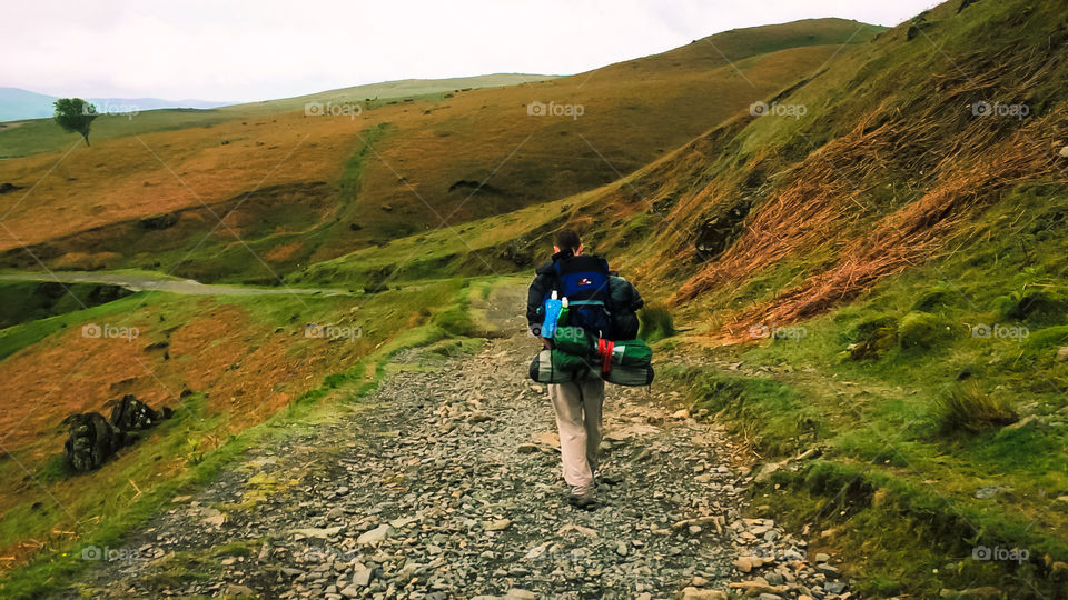 A backpacker makes an early morning start on the day’s hike through scenic rolling hills of the Lake District 