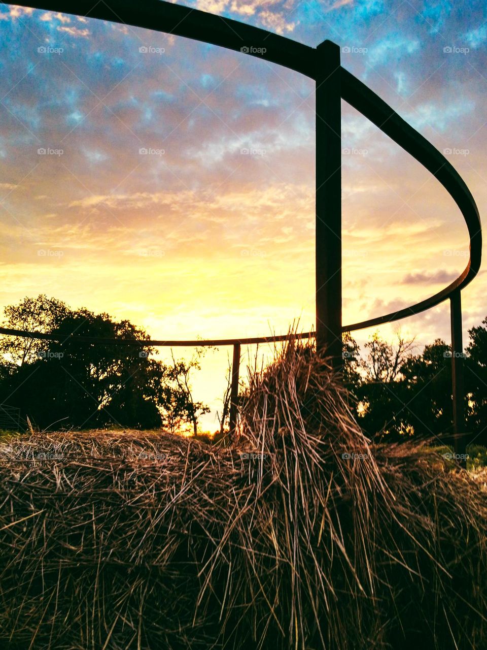 Sunset thru a Hay Ring with a colorful cloud filled sky on a countryside farm