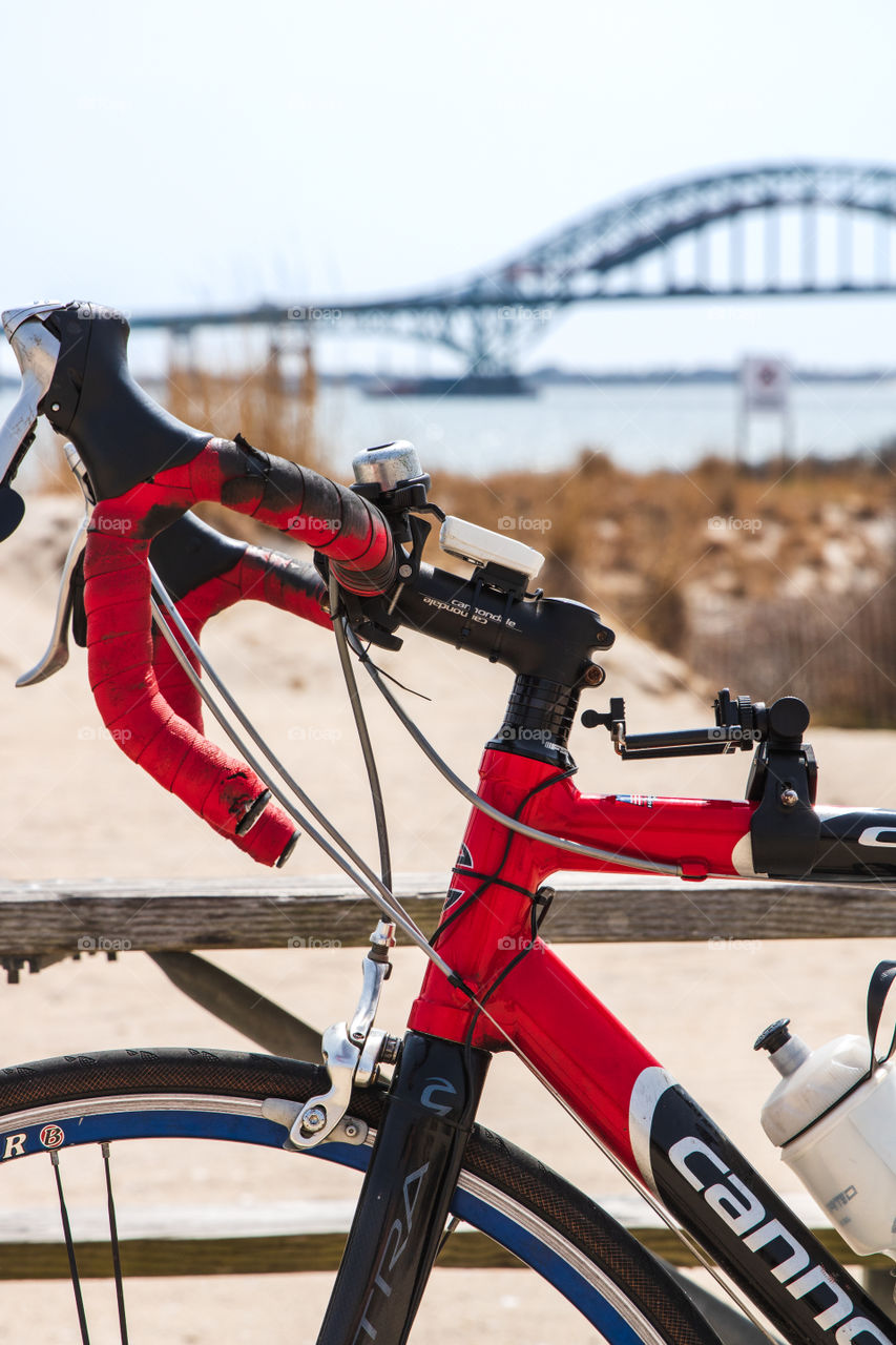 Portrait of a red men’s bike with worn handlebar tape with an arch bridge in the background