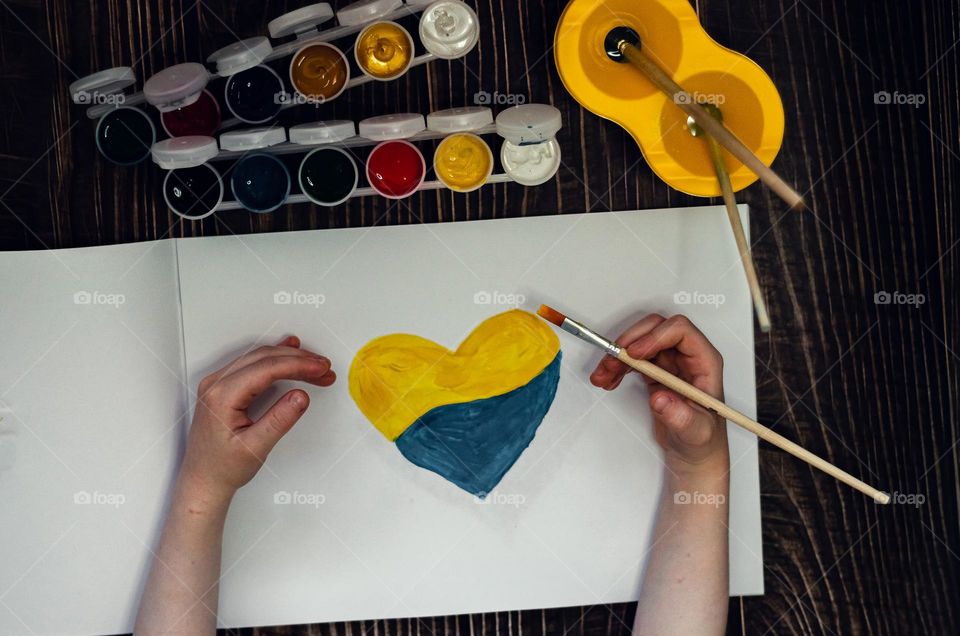 The child painted a heart with yellow and blue paints.