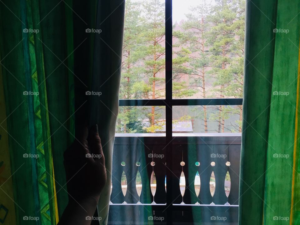 Hand pulling apart green curtains of the window revealing forest