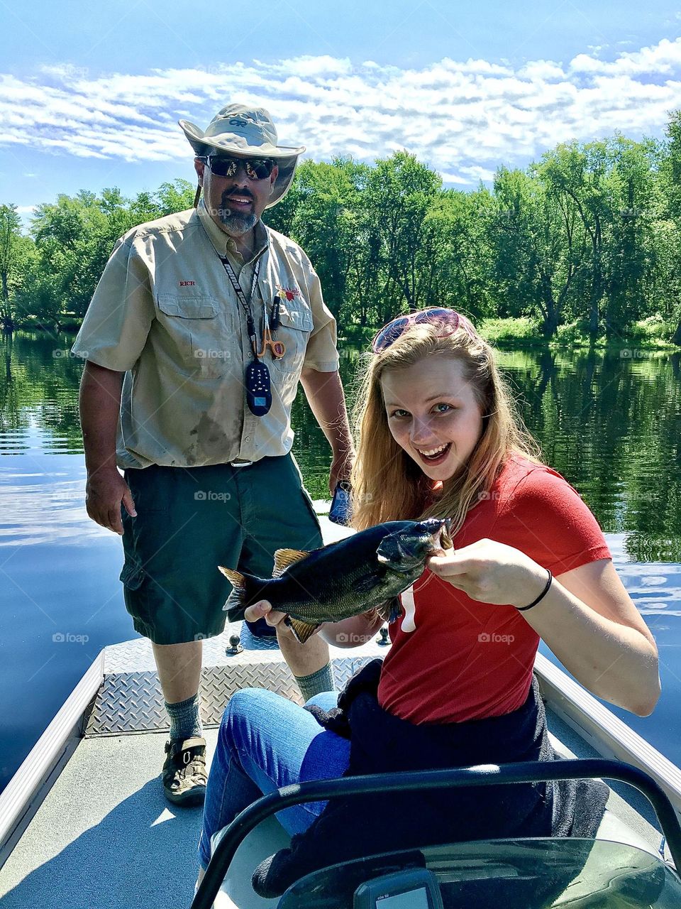 A Summer fishing trip in Maine, where a girl shows her smallmouth bass catch on a sunny day.