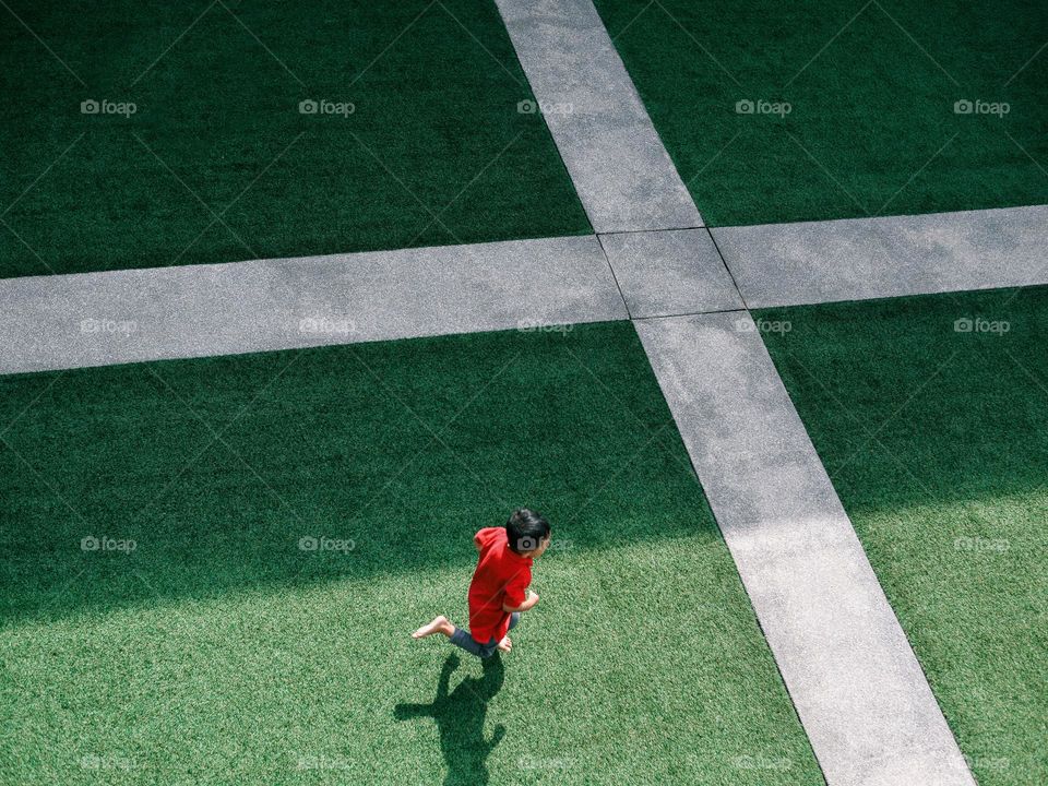 A boy in red running on an astro turf plaza