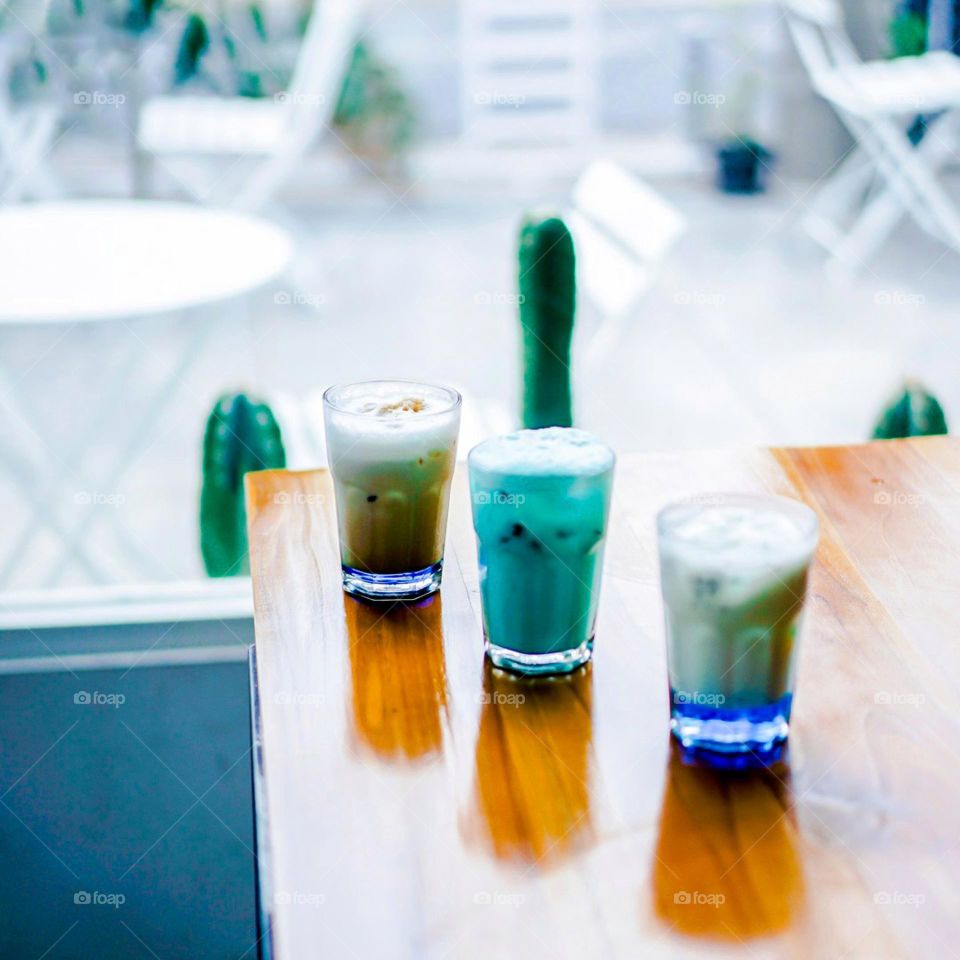 Three glasses of drink on a cafe table. Drink. Beverages. Café. Table. Wood. Wooden table. Photography. Glass. Cold. Ice. Three. Fresh. Freshness. In a line. Desserts. Cold drinks. Estetik. Tranquil.