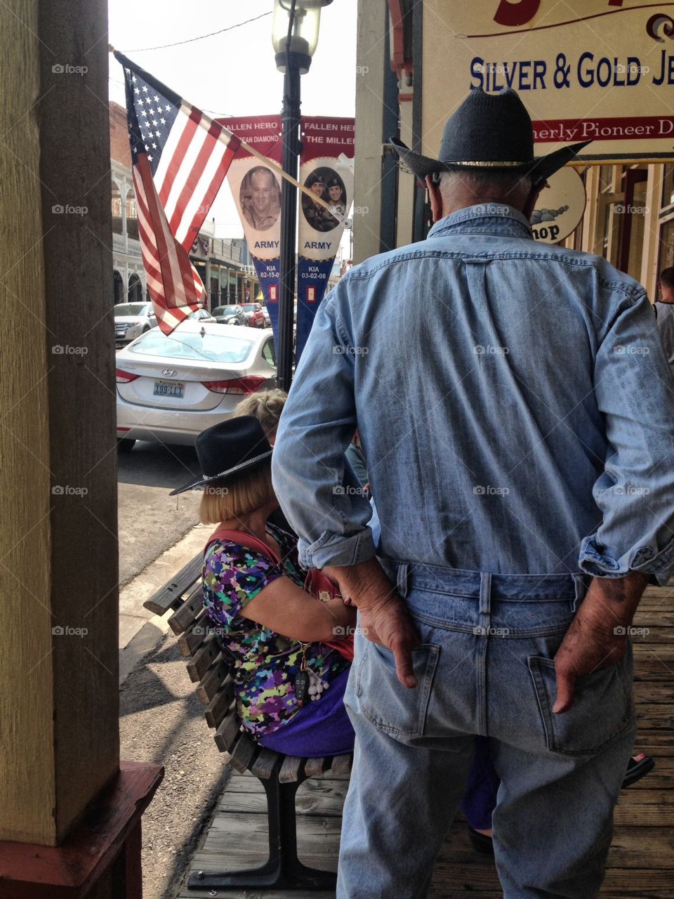 Back view elderly cowboy in town and socialising with people sitting in bench 