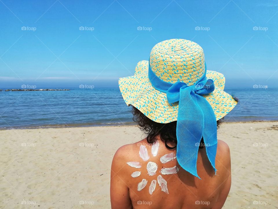 Woman with hat and sun cream looks at the sea
