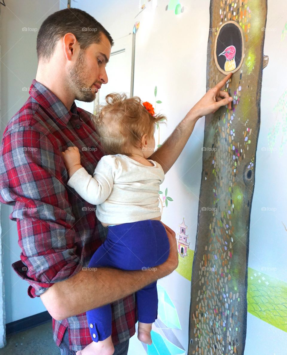 Father pointing painted bird on wall with daughter